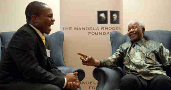 An image of Nelson Mandela sitting opposite a Rhodes Scholar. They are sitting in armchairs, both smiling and in the middle of a conversation. In the background is a banner that says 